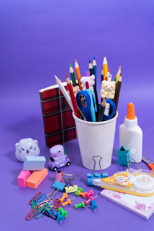 Colorful pencils, erasers, glue, scissors and other stationery items are arranged neatly on a purple surface, perfect for back-to-school projectsの写真素材