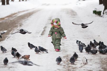 Child runs through a flock of pigeons on the square in winter city parkの写真素材