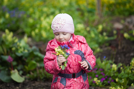 Little girl holding yellow flower bouquet in spring gardenの写真素材