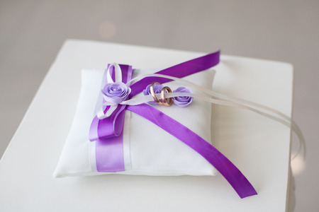 Golden wedding rings on decorated little pillow with purple ribbonsの写真素材