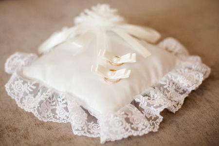 Golden wedding rings on decorated little white pillow on sofa. Marriage conceptの写真素材