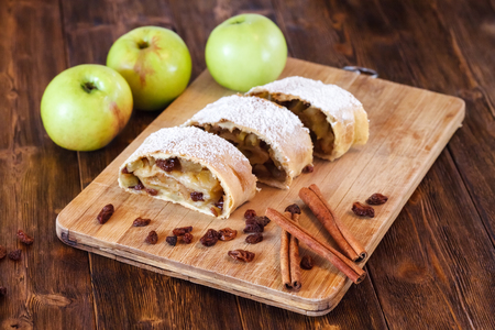 Apple strudel with icing sugar, cinnamon sticks, raisins, wooden backgroundの写真素材
