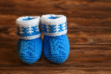 Blue hand made crochet baby booties on wooden background, copyspace, closeup