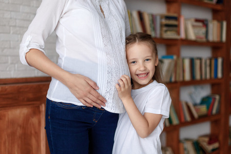 Cute little girl hugging belly of her pregnant mother, listening, closeupの写真素材