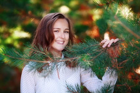 Portrait of smiling pretty girl in green spruce branches, autumn parkの写真素材