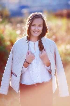 Pretty smiling caucasian girl in sunlight. Colorful autumn park. Vertical shoot