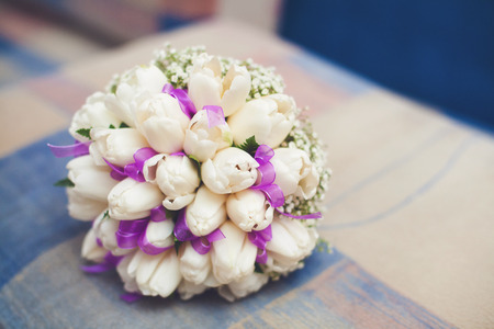 Beautiful white wedding bouquet of tulips with purple ribbon on sofaの写真素材