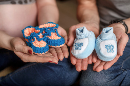 Cute small blue knitted baby booties on hands. Pregnancy concept