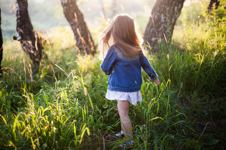 Little girl with long hair running, meadow, sunset. View from backの写真素材