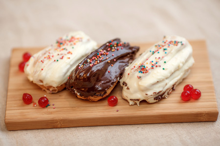 Three eclair cakes with white and brown cream on wooden board