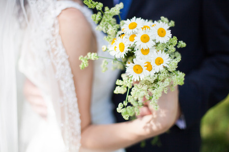 Beautiful yellow chamomile bouquet in hands of bride and groomの写真素材