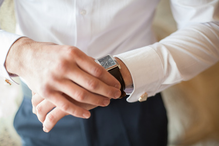 The groom in white shirt puts on a watch, closeup