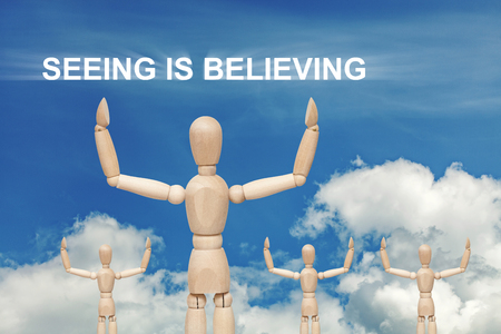 Wooden dummy puppet on sky background with words SEEING IS BELIEVING. Abstract conceptual imageの写真素材