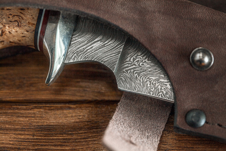 Hunting damascus steel knife handmade in sheath on a brown wooden background, closeupの写真素材