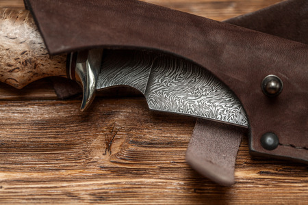 Hunting damascus steel knife handmade in sheath on a brown wooden background, closeupの写真素材