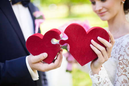Bride and groom holding big puzzle red hearts, wedding concept, closeupの写真素材
