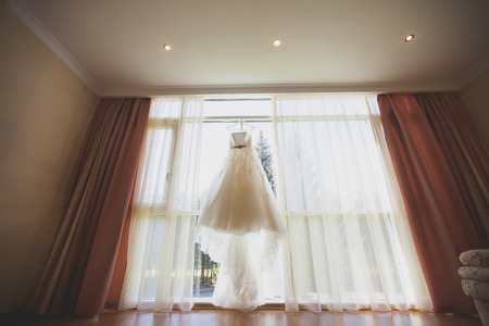 Bridal gown in hotel room, beautiful wedding dress hanging in the bride's roomの写真素材