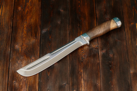 Big hunting steel knife handmade on a brown wooden background, closeupの写真素材