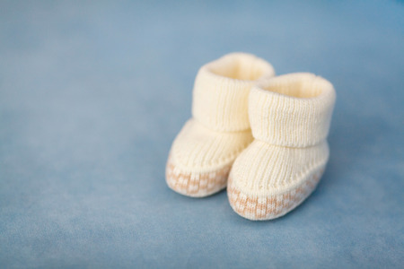 White crochet baby booties on blue background, closeup, selective focusの写真素材