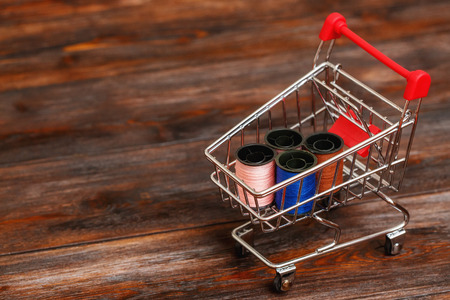 Mini shopping cart with thread spools. Abstract conceptual image