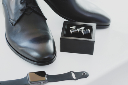Black leather male dress shoes, cufflinks and watch on white background