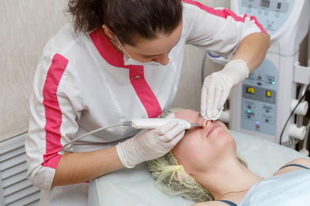 Cosmetologist doing procedure cleaning of face with ultrasonic scrubber in beauty salonの写真素材