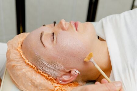Woman getting pink face peeling mask in spa beauty salon by beautician