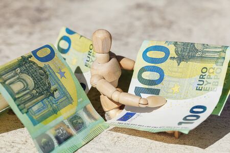 Wooden dummy puppet holding hundredth euro banknotes. Money or business concept. Abstract conceptual imageの写真素材