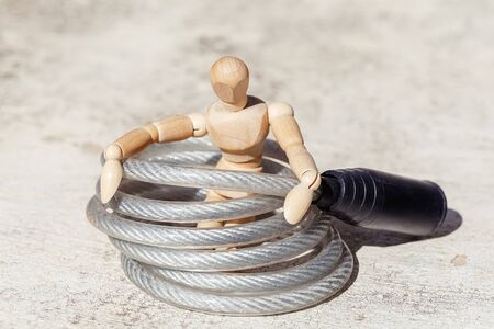 Wooden dummy puppet in long bike lock on white concrete background. Abstract conceptの写真素材