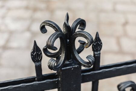 Black painted iron forged fence with stone wall background, closeup