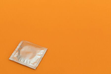 A foil condom package on orange background with copyspaceの写真素材