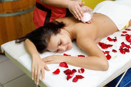 Masseur applying cream to woman's back. Rose petals. Massage in spa salonの写真素材