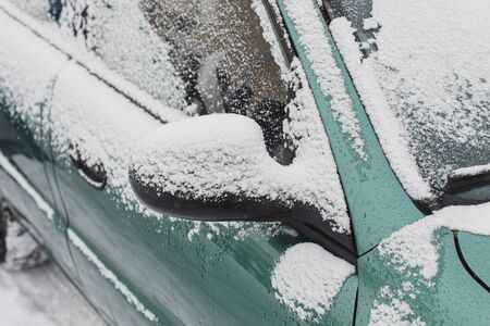 Closeup of snow covered mirror of green car in winterの写真素材
