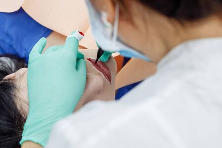 Woman having permanent makeup on lips in beauty salon. Cosmetologist in gloves applying tattoo with machine, macro viewの写真素材