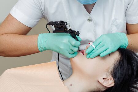 Woman having permanent makeup on lips in beauty salon. Cosmetologist in gloves applying tattoo with machine, macro viewの写真素材