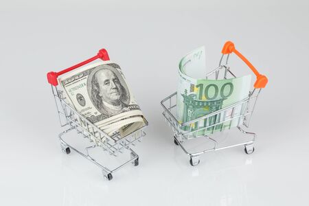 Mini shopping carts with dollar and euro banknotes on gray background, money or currency conceptの写真素材