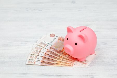 Pink piggy money box on pile of russian rouble banknotes on gray wooden background, currency concept