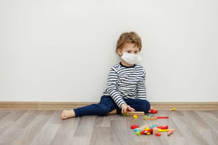 Little boy in medical face mask sitting and playing. Stay home concept, quarantine campaign from Coronavirus Covid-19の写真素材