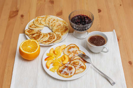 Fritters or pancakes on white plate served with jam, fruits and coffee