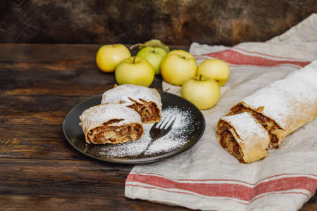 Apple strudel with icing sugar and raisins on black plate, wooden backgroundの写真素材