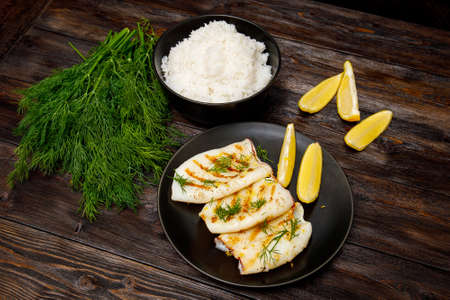 Grilled squid with a rice, lemon and greens on dark wooden backgroundの写真素材