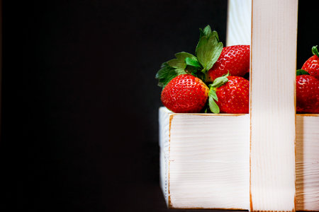 Ripe strawberries. Red berry in a white basket on a black blurred background. Place for text.の写真素材
