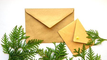 Brown envelope on a white background and a sprig of evergreen cypress. Christmas background. Flat...