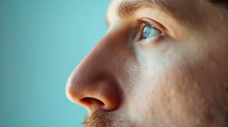 A young male model with blue eyes, a beard, and a pensive expression on his face. He is looking away from the camera and has a neutral expression. The background is a light blue color.の素材