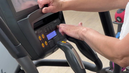 An elliptical cross-trainer is programmed for cardio training by a womans hand. Hands of an elderly...