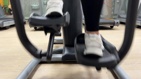Close-up video: moving legs in white sports shoes on the exercise machine. Mature woman training on...