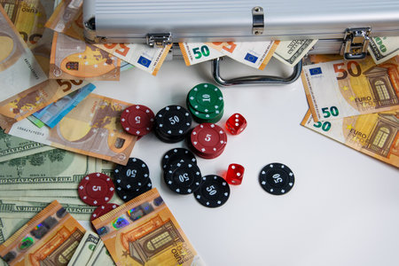 A close-up image of poker chips and dice with Euro and US Dollar bills scattered around them on a...
