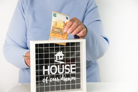 A persons hand puts a 50 Euro bill into a box labeled House of Our Dreams.の写真素材
