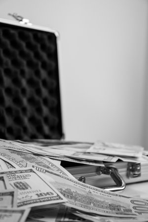 A black and white image of an open metal briefcase with stacks of cash spilling out.の写真素材