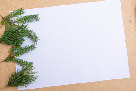 A blank sheet of paper lies on a wooden surface, accompanied by fresh evergreen branches. This serene setup is perfect for winter crafting and creative projects.の写真素材